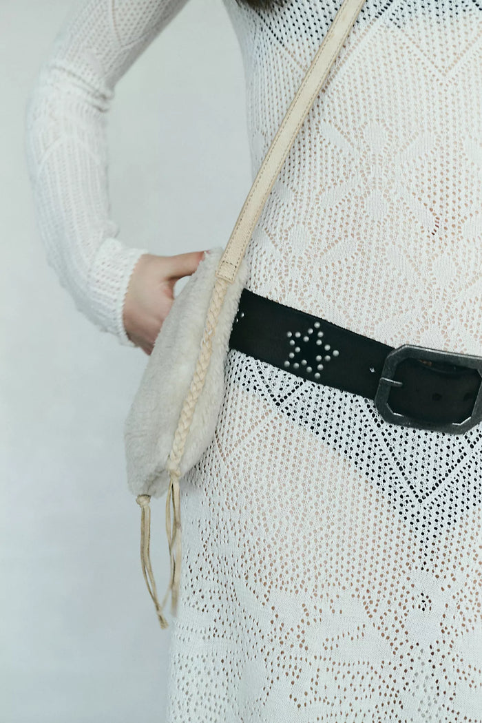 Person wearing a white textured sweater with a black belt and beige bag on a light gray background. Free People Starcrossed Studded Belt
